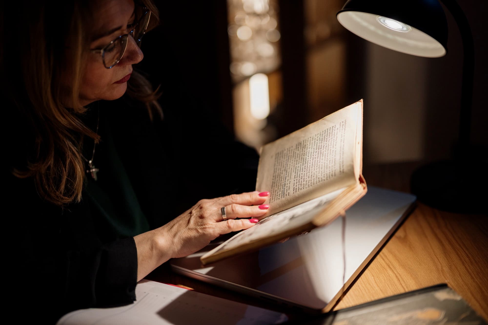 Pessoa lendo com atenção sob luz de mesa, à noite.